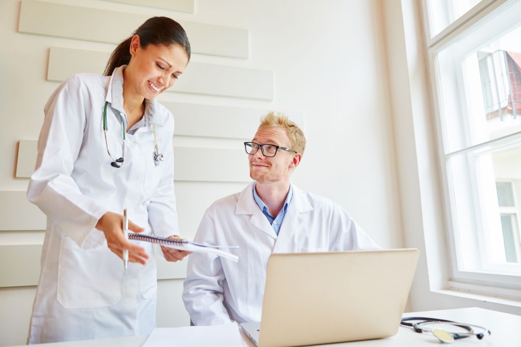 Smiling Healthcare Workers Discussing Over Note Pad At Medical Clinic